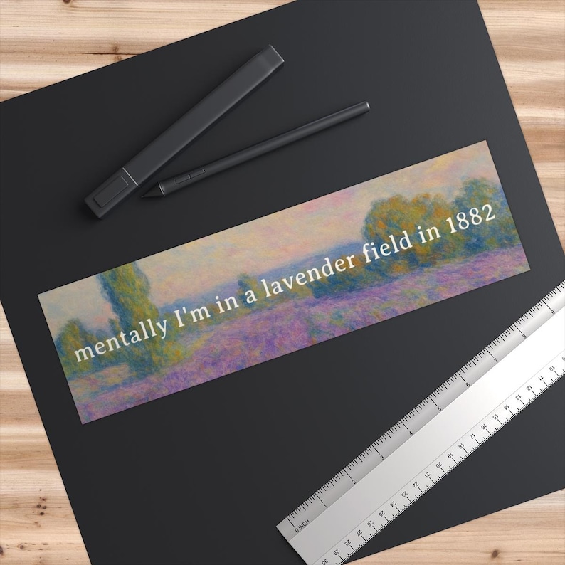 May include: A rectangular bookmark with a lavender field painting and the text "mentally I'm in a lavender field in 1882" in white. The bookmark is on a black surface with a ruler and pen.