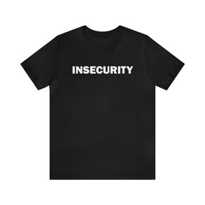 May include: Black t-shirt with the word "INSECURITY" printed in white on the front.