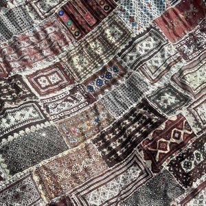 May include: A patchwork textile featuring a variety of rectangular pieces. The pieces display detailed patterns in shades of brown, beige, and burgundy. The design includes geometric shapes and floral motifs.