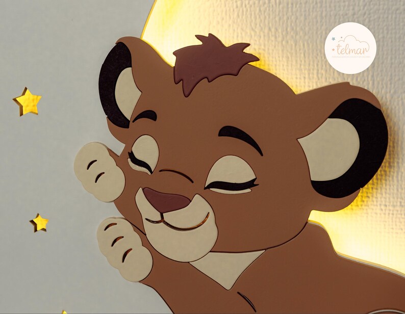 May include: A wooden wall decoration featuring a cartoon lion cub with closed eyes, a light brown mane, and a light beige face. The lion cub is set against a yellow crescent moon and surrounded by yellow star cutouts. The Telman logo is in the upper right corner.