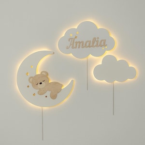 May include: White wooden wall decor with a crescent moon, a cloud, and a nameplate. The moon has a sleeping bear and stars. The nameplate says "Amalia".