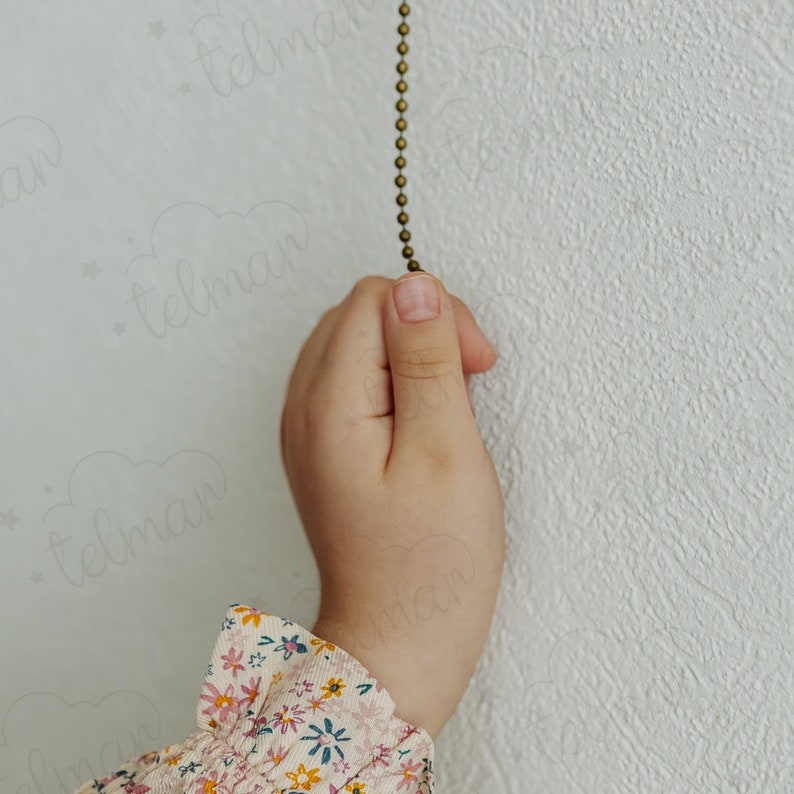 May include: A child's hand reaches up to pull a gold chain hanging from a white wall.
