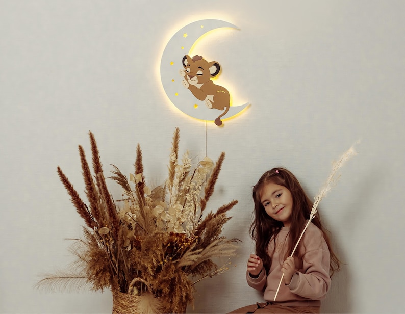 May include: A wooden crescent moon night light with a sleeping lion cub design. The light is warm and inviting, perfect for a child's room. The light is hanging on a wall.