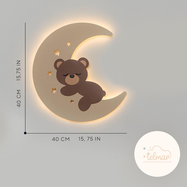 May include: A beige wooden crescent moon night light with a brown bear sleeping on it. The moon has cut-out stars and a warm white glow. The light measures 15.75 inches in diameter.