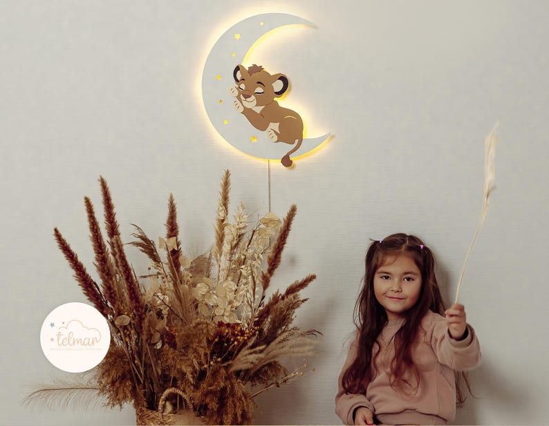 May include: A wooden night light shaped like a crescent moon with a sleeping lion cub design. The moon is white with yellow stars and a warm glow. The image also shows a young girl holding a plant.