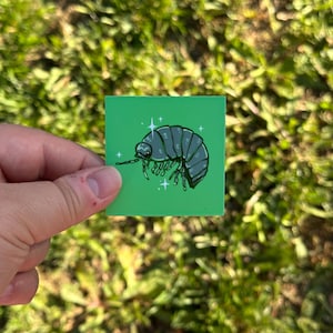 May include: A square sticker with a vibrant green background featuring a centred illustration of a dark grey pill bug or woodlouse. The insect is depicted with multiple legs and segments, accented by small white star-shaped sparkles around its body.