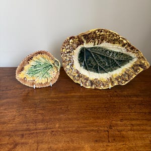 May include: Two ceramic leaf-shaped serving dishes. The larger dish has a dark green centre, a white border, and a textured brown and yellow edge. The smaller dish has a green and yellow centre with a brown and yellow edge.