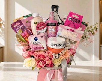 May include: A gift arrangement in a pink box featuring a collection of skincare products including Vaseline, Dr. Rashel Shine spray, and Fruit Brightening cream, surrounded by artificial pink and white roses and decorative floral accents.