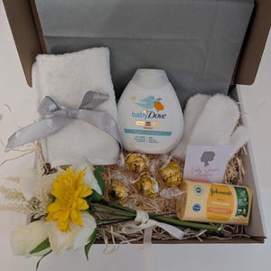 Puede incluir: Una caja de regalo blanca llena de art&iacute;culos para el cuidado del beb&eacute;, que incluyen una toalla blanca, una botella de loci&oacute;n Baby Dove, una toallita blanca, un peque&ntilde;o ramo de flores amarillas y blancas, una caja de chocolates y una barra de jab&oacute;n para beb&eacute;s Johnson's. La caja tambi&eacute;n incluye una peque&ntilde;a tarjeta con el texto "Lady Grace Hamper".