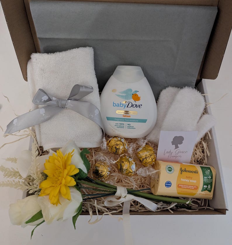 Puede incluir: Una caja de regalo blanca llena de art&iacute;culos para el cuidado del beb&eacute;, que incluyen una toalla blanca, una botella de loci&oacute;n Baby Dove, una toallita blanca, un peque&ntilde;o ramo de flores amarillas y blancas, una caja de chocolates y una barra de jab&oacute;n para beb&eacute;s Johnson's. La caja tambi&eacute;n incluye una peque&ntilde;a tarjeta con el texto "Lady Grace Hamper".