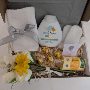 Puede incluir: Una cesta de regalo llena de art&iacute;culos para el cuidado del beb&eacute;, que incluyen una botella de loci&oacute;n para beb&eacute;s, una toallita, una pastilla de jab&oacute;n y un peque&ntilde;o ramo de flores amarillas y blancas.