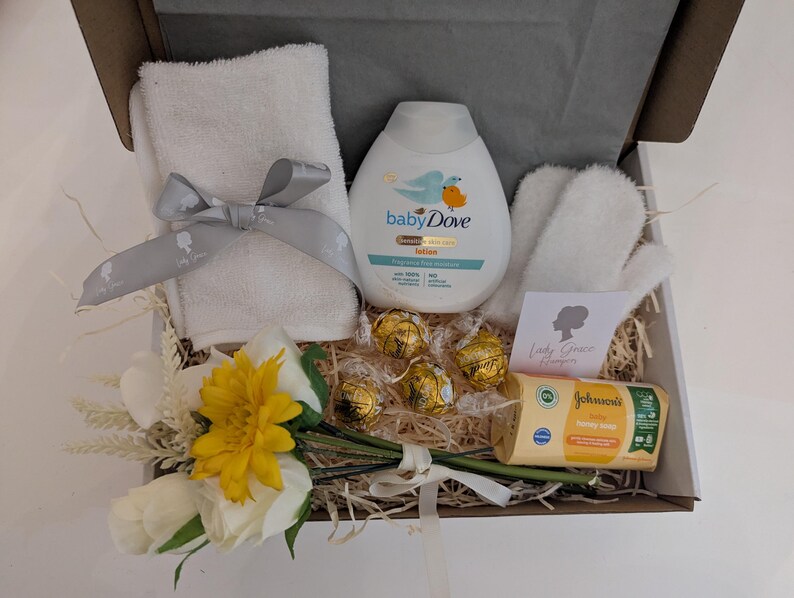 Puede incluir: Una cesta de regalo llena de art&iacute;culos para el cuidado del beb&eacute;, que incluyen una botella de loci&oacute;n para beb&eacute;s, una toallita, una pastilla de jab&oacute;n y un peque&ntilde;o ramo de flores amarillas y blancas.