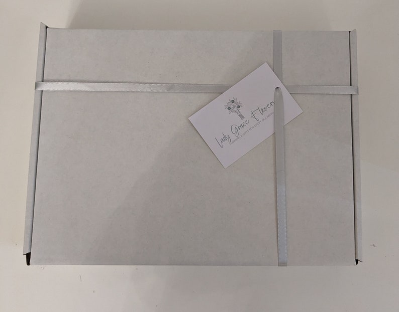May include: A white gift box with a silver ribbon and a business card that reads "Lady Grace Flowers" with a floral design.