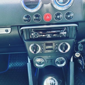 May include: Car dashboard featuring a Sony stereo, air vents, and control buttons. The black dashboard has silver accents, including circular dials and a red hazard light button. The gear shift is visible. The car's interior is black.