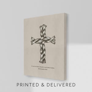 May include: A canvas print featuring a detailed illustration of a cross made from intertwined rope. The artwork is in grayscale, set against a beige background. The text "A cord of three strands is not easily broken. Ecclesiastes 4:12" is printed below the cross.