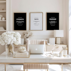 May include: Three framed prints with inspirational words: "Strength," "Faith," and "Courage." The black and white prints are displayed above a white desk with a laptop, flowers, and decorative items. The frames have gold trim.