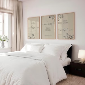 May include: Three framed wall art pieces with inspirational quotes in a bedroom setting. The art features text in elegant script with botanical accents. The bed is made with white linens, and a nightstand with a lamp is visible.