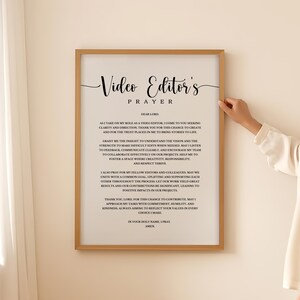 Puede incluir: Una oración imprimible para editores de video. La oración está enmarcada en un marco dorado e impresa en papel blanco. El texto dice "Oración del editor de video" e incluye una oración para la claridad, la dirección y la fuerza en el papel de un editor de video.