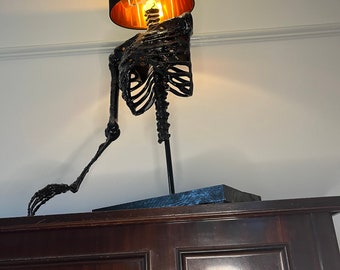 May include: A black skeleton lamp with a black lampshade and a gold interior. The lamp is on a dark wood surface.