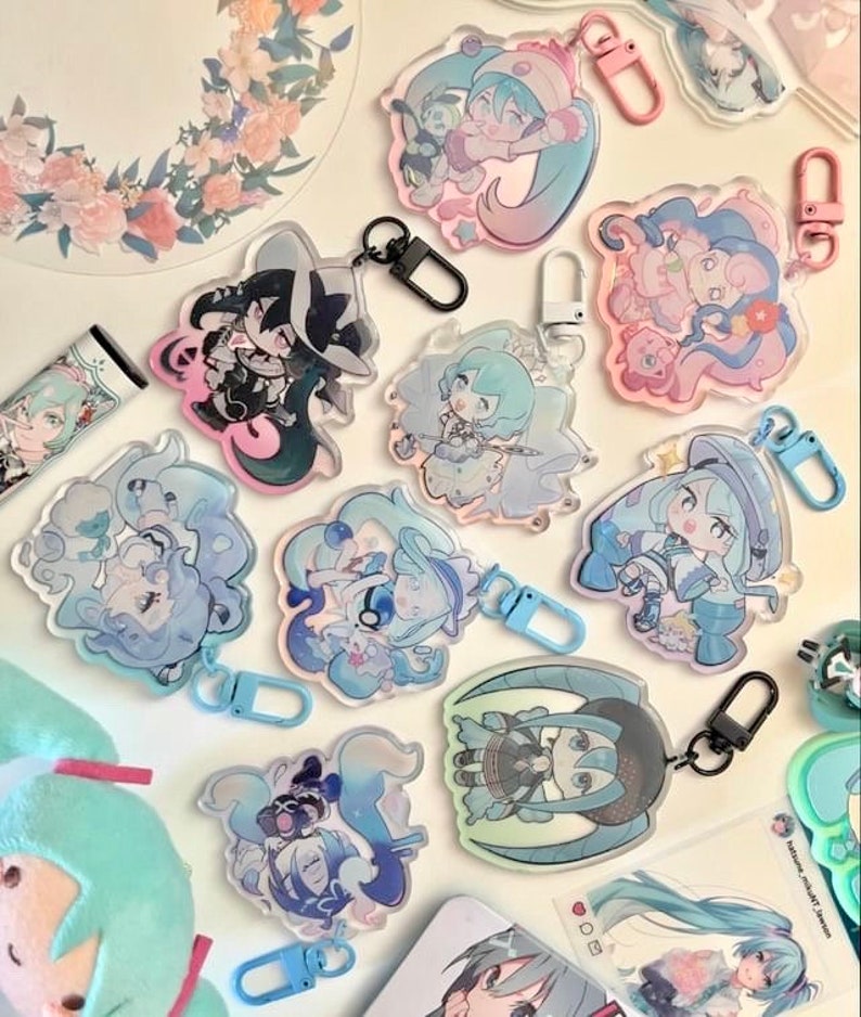 May include: A collection of 11 colorful anime character keychains with clear acrylic backgrounds. The keychains feature various characters with different poses and expressions. The keychains are attached to silver and black metal rings.