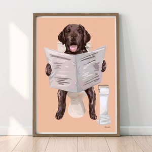 Könnte beinhalten: Ein brauner Labrador Retriever sitzt auf einer Toilette, liest eine Zeitung und hat eine Rolle Toilettenpapier daneben. Der Hund trägt ein weißes Halsband und hat einen rosa Hintergrund.