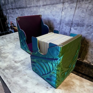 May include: A green, blue, and purple iridescent card box with a deck of cards inside. The box is made of plastic and has a textured design.