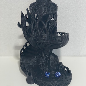 Può includere: Una torre per dadi nera con un intricato design ad albero. Presenta una scala a chiocciola, una piccola piattaforma e una parte superiore decorativa. Sono visibili due dadi blu con numeri bianchi.