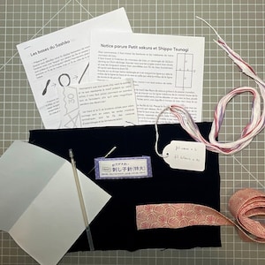 Könnte beinhalten: Ein Sashiko-Stickset mit einem rosa-weißen Blumenstoff, einem schwarzen Stoff, einem weißen Stoff, einer Nadel, einer Garnrolle, einem Etikett mit dem Text "fil care x 6 fil delave x 10" und einer Packung mit der Aufschrift "刺し子針(特大)".