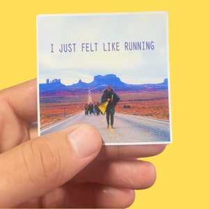 May include: A sticker with a photo of a person running down a road in a desert landscape. The text "I JUST FELT LIKE RUNNING" is printed in purple on the sticker.