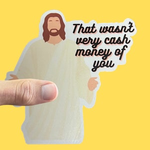 May include: A white sticker with a cartoon image of Jesus in a white robe with long brown hair and a beard. The text "That wasn't very cash money of you" is written in black cursive font.
