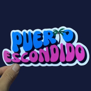 May include: A sticker with the text "PUERTO ESCONDIDO" in a blue and pink font with a palm tree graphic. The sticker has a white outline.