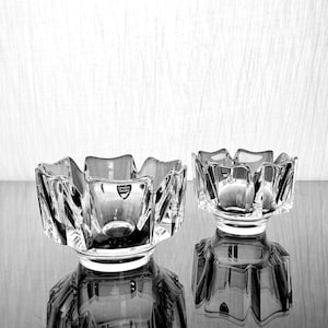 Peut inclure: Deux bols en verre transparent avec un design en forme de fleur. Les bols ont un extérieur facetté et une base ronde. Les bols sont posés sur une surface réfléchissante. Les bols portent une étiquette "Orrefors Sweden".