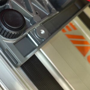 Puede incluir: Primer plano de un trípode de cámara plateado y negro con un tornillo roscado para sujetar una cámara. El trípode tiene una perilla negra para ajustar la altura.