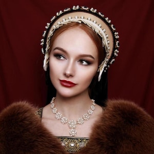 May include: A woman wearing a pearl necklace and a large, ornate headpiece with pearls and black velvet. She is wearing a brown fur stole and has a red lip.