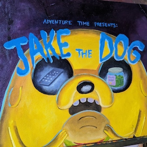 May include: A yellow cartoon dog with blue eyes and a blue mouth. The dog is holding a brown burger in its paws. The text "JAKE THE DOG" is written in blue letters above the dog. The text "ADVENTURE TIME PRESENTS" is written in white letters above the text "JAKE THE DOG".