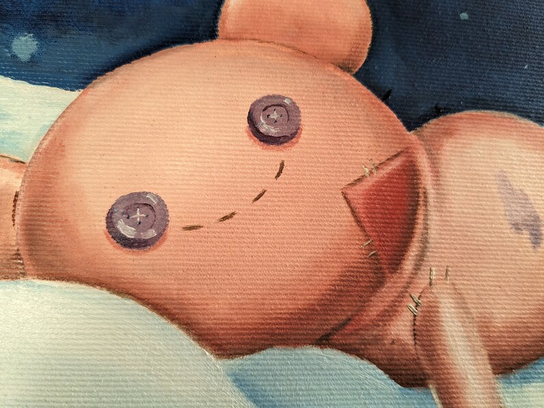 May include: A close-up of a painted teddy bear with button eyes and stitched details. The bear is a light peach color with a red patch and a stitched smile. The background is a dark blue with white accents.