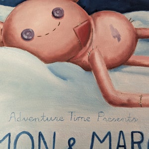 May include: A pink plush toy with button eyes and stitched details, lying on a fluffy white surface. The toy has stitched limbs and a stitched smile. The text "Adventure Time Presents SIMON & MARCY" is visible in the image.