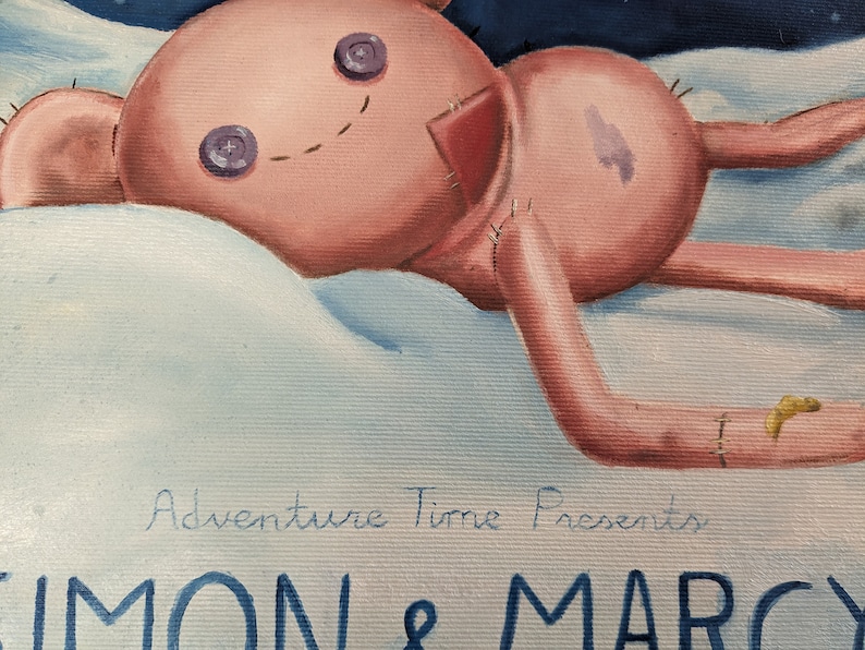 May include: A pink plush toy with button eyes and stitched details, lying on a fluffy white surface. The toy has stitched limbs and a stitched smile. The text "Adventure Time Presents SIMON & MARCY" is visible in the image.