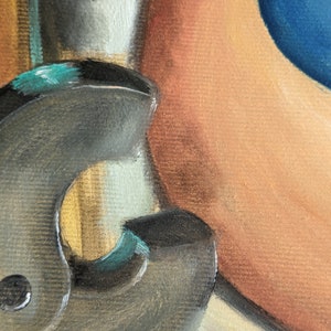 May include: A close-up of a black metal object with a teal accent. The object has a rounded shape and a textured surface. It is partially obscured by a light brown background.