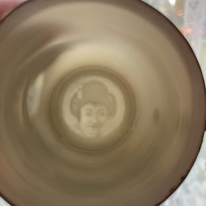 Peut inclure: Intérieur d'une tasse à thé vintage avec un portrait estompé de femme. L'intérieur de la tasse est beige clair, avec un bord marron plus foncé. Le portrait est au centre de la tasse.