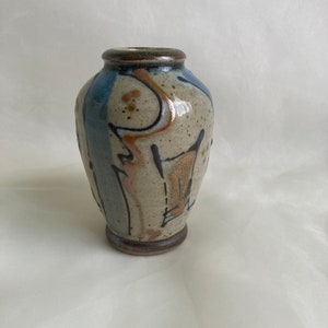 Op de afbeelding: Een kleine, handgeschilderde keramische vaas met een abstract ontwerp in blauw, bruin en beige. De vaas heeft een rond lichaam en een licht uitlopende opening.