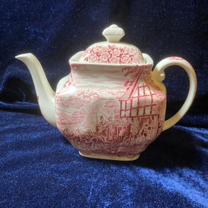 May include: A white teapot with a red and white floral design. The teapot has a square body and a lid with a knob. The teapot is decorated with a scene of a horse-drawn carriage and people.