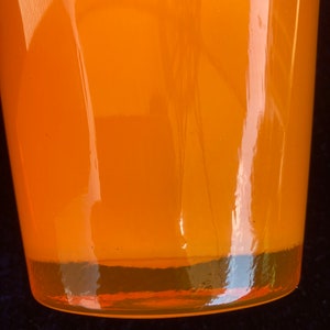 May include: A bright orange glass vase with a rounded bottom and a smooth, shiny surface.