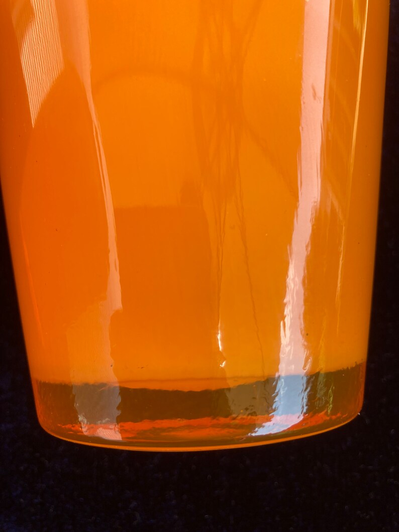 May include: A bright orange glass vase with a rounded bottom and a smooth, shiny surface.