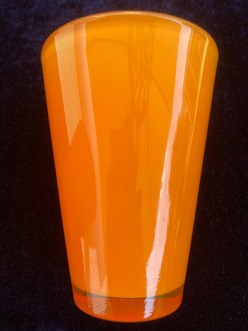 May include: A bright orange glass vase with a rounded bottom and a flared top.