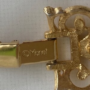 May include: A gold-toned metal bracelet with a clasp that reads "&copy;Monet". The bracelet has a decorative, ornate design.