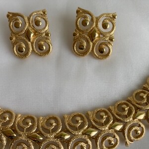 May include: A gold-tone necklace and earrings set with a geometric design featuring interlocking circles and a textured finish.