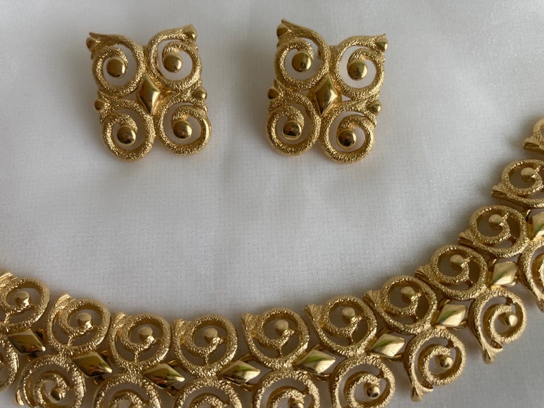 May include: A gold-tone necklace and earrings set with a geometric design featuring interlocking circles and a textured finish.