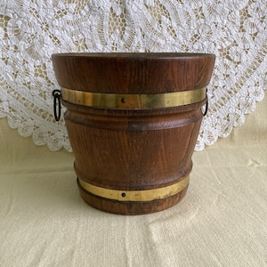 Pode incluir: Um balde de madeira com duas faixas de latão e alças de metal. O balde é castanho e tem um acabamento em madeira natural.