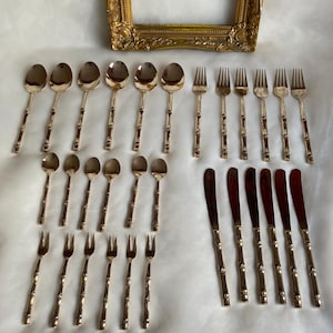 Könnte beinhalten: Ein Set aus vergoldetem Besteck mit Griffen im Bambus-Stil. Das Set enthält Löffel, Gabeln und Buttermesser.